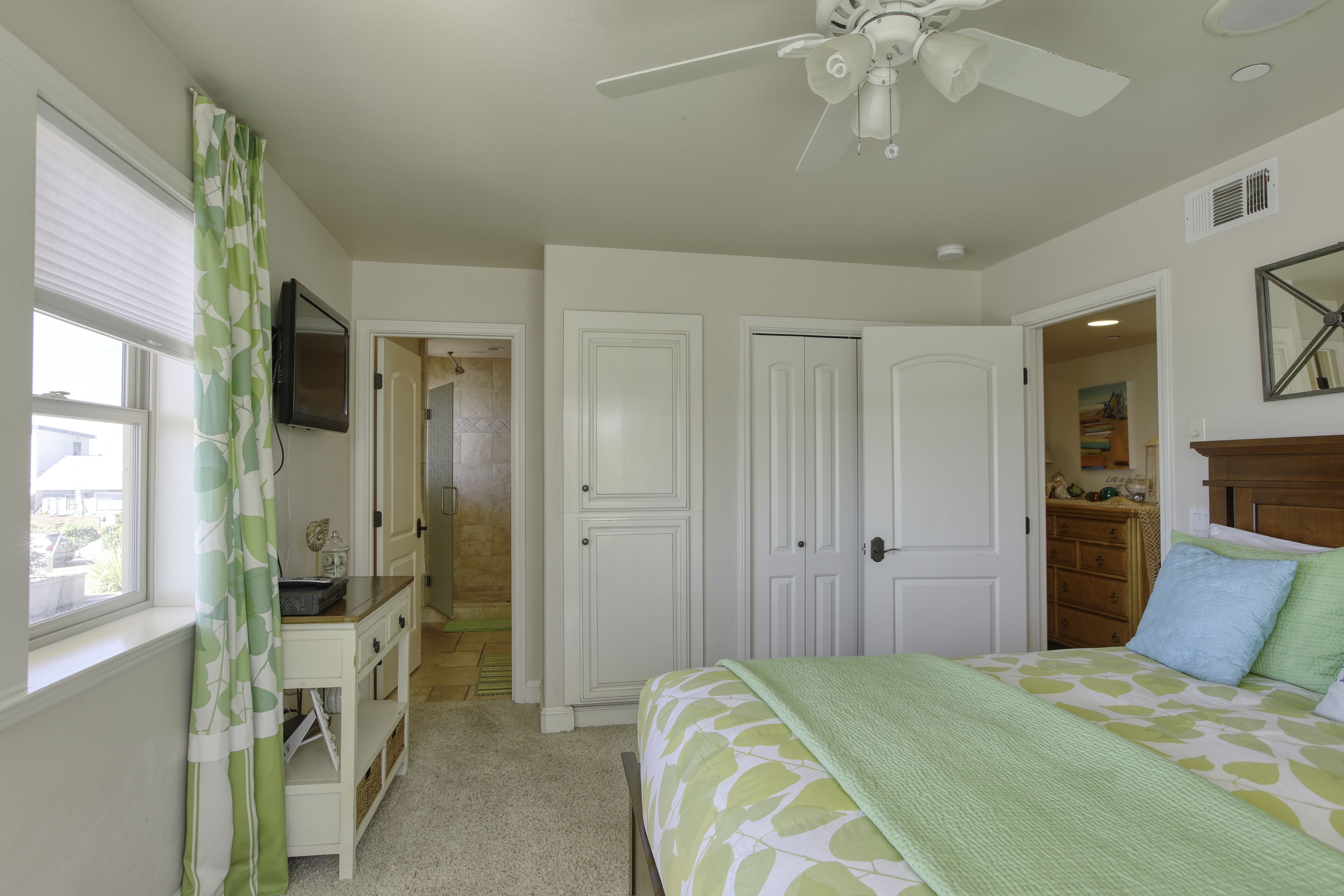 A bedroom with a bed, a desk, a chair, a ceiling fan, and a dresser.