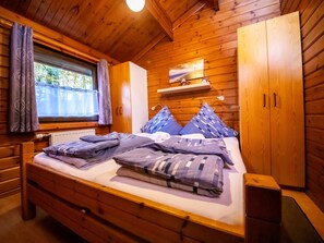 Ein Schlafzimmer in einer Holzhütte mit Bett, Kleiderschrank, einer Ablage mit Dekoration und einem Fenster mit Vorhängen.