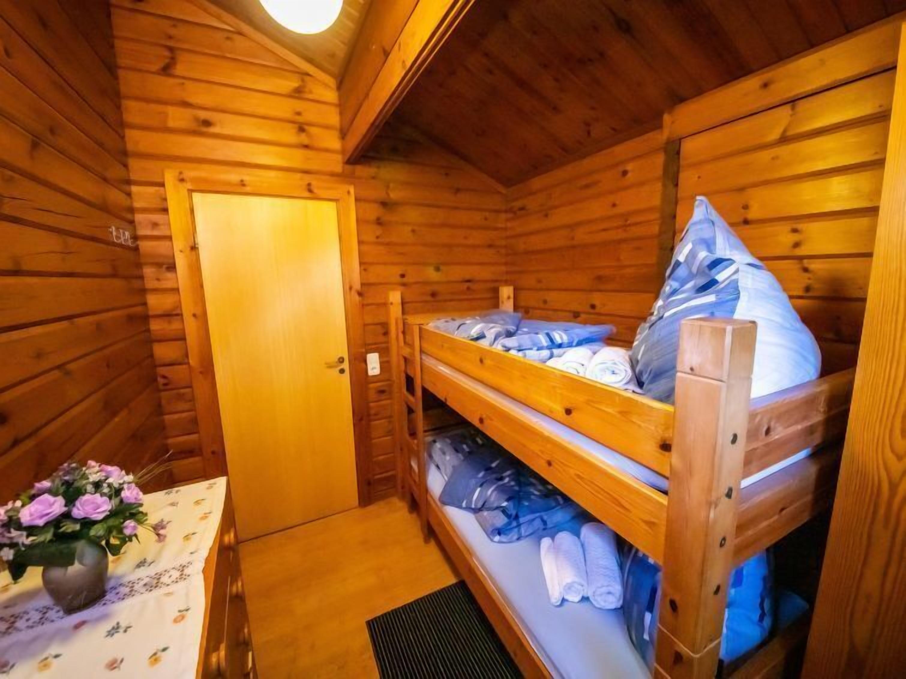 Ein Zimmer in einer Holzhütte mit einem Etagenbett, einem kleinen Tisch und einer Blumenvase sowie einer Tür.