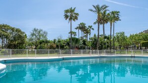 A clear blue pool surrounded by a white fence, with palm trees and greenery in the background. - Apartment (Torremolinos)