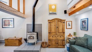 A cozy living room with a white wood-burning stove, a green sofa, and a wooden cabinet. - Bright and Airy Condo, Sleeps 4! - Creekside #103 by Bear Valley Vacation Rentals (Arnold)