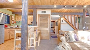 Un intérieur chaleureux avec un plafond en bois, un coin cuisine, un canapé avec des coussins et un escalier.