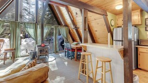 L’intérieur chaleureux d’un chalet comprend un coin repas, une cuisine et une grande fenêtre donnant sur un paysage enneigé.