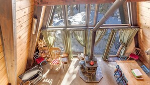 L’intérieur chaleureux d’un chalet avec une grande fenêtre, des murs en bois, une cheminée et un coin repas.