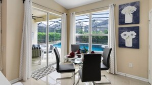 Un coin repas avec une table en verre, des chaises noires et une vue sur une piscine, visible à travers de grandes fenêtres.