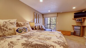 A bedroom with a large bed, a television on a shelf, a refrigerator, and a window with a view. - Ski-In Ski-Out Center Village Hotel Room - CM217 by Redawning (Copper Mountain)
