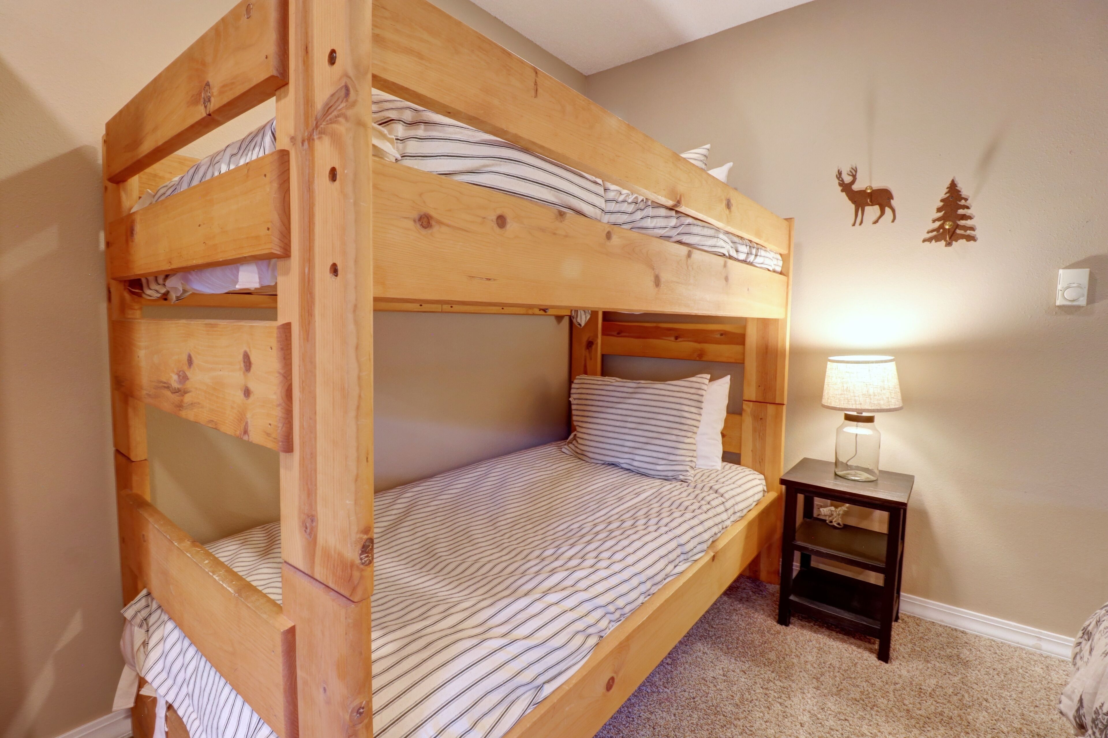 A bunk bed with striped bedding, a small bedside table with a lamp, and wall decorations of a deer and a tree.