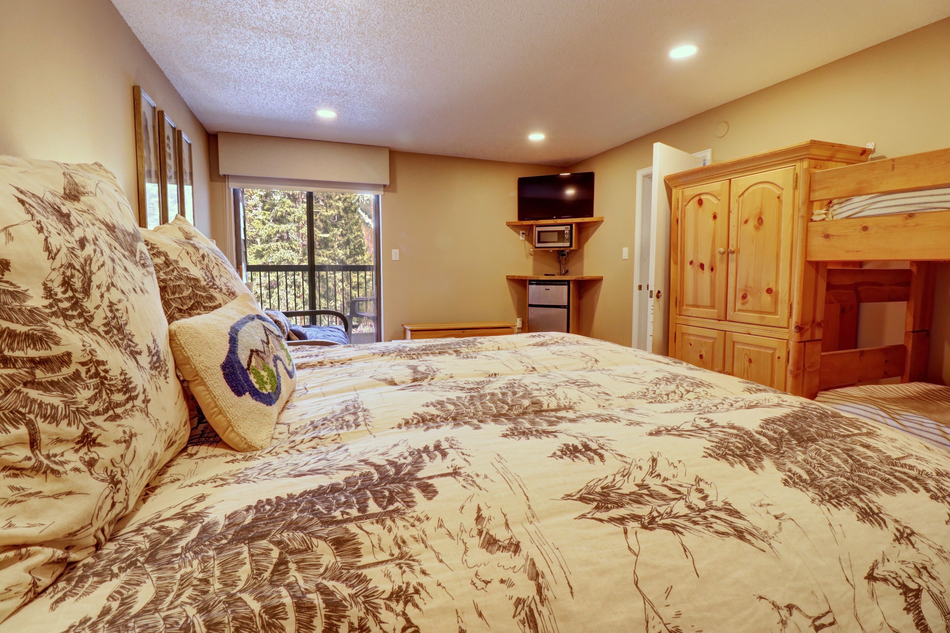 Un dormitorio con cama, televisor, armario y ventana con vista a árboles.
