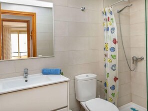 Een badkamer met een wit wastafel, een toilet en een douche met een vrolijk gordijn met een vispatroon.