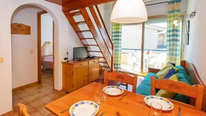 Un coin repas avec une table et des chaises en bois, un luminaire suspendu et une vue sur un balcon doté d’une balustrade.