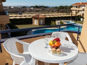 Een balkon met een zwembad, witte stoelen, een tafel met een schaal fruit en glazen, en uitzicht op het landschap.