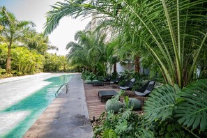 A poolside area with a wooden deck, lounge chairs, and tropical plants. - LUX & unique 3BR condo by the US Consulate, North Mérida (Mérida)