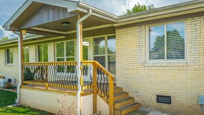 Een gelijkvloers huis met een overdekte veranda, een houten trap en een gevel van baksteen.