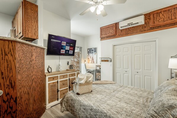 A bedroom with a wooden wardrobe, a flat-screen TV mounted on the wall, a ceiling fan, and a white door.