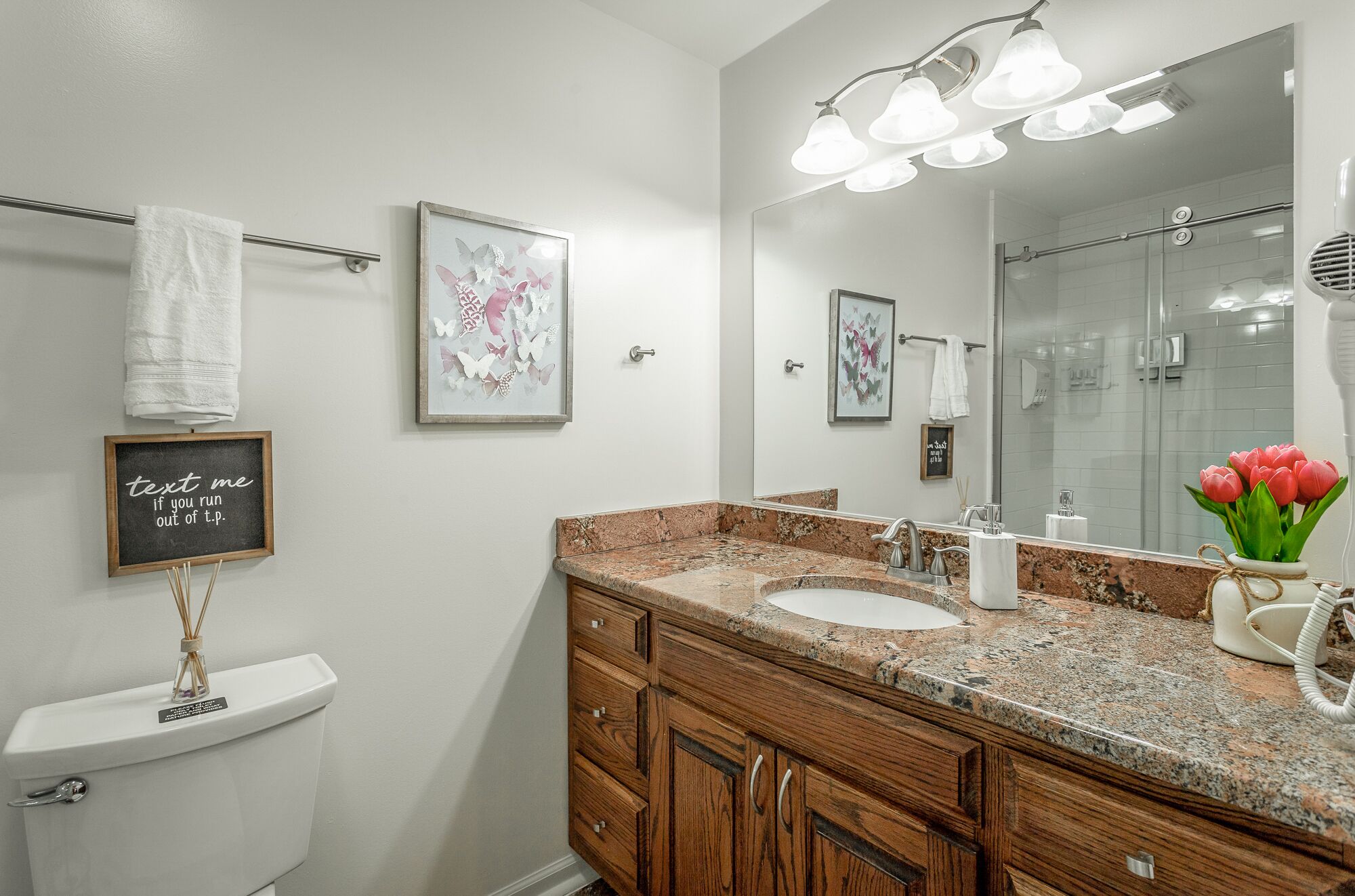 A bathroom with a white toilet, wooden vanity, granite countertop, and a large mirror.