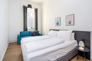 Ein Hotelzimmer mit einem Doppelbett, einem blauen Sofa, einem kleinen Tisch mit Lampe und zwei gerahmten Bildern an der Wand.