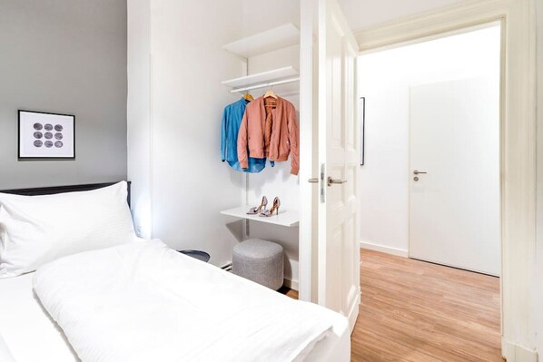 A bedroom with a bed, a wardrobe, a small stool, and a door leading to another room. - 1-Bedroom Apartment 70sqm with a cozy living room(3) (Mitte / Wedding (Berlin))