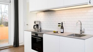 A modern kitchen with white cabinets, a built-in oven, a coffee maker, and a wine bottle on the counter.