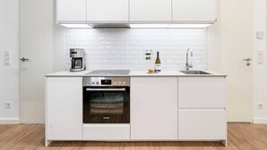 A compact kitchen with white cabinetry, a built-in oven, a coffee maker, and a wine bottle on the counter.