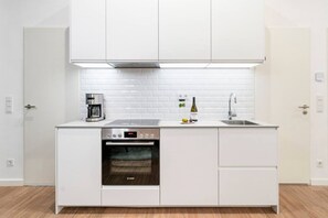 Uma cozinha moderna com armários brancos, forno embutido, cafeteira e uma garrafa de vinho no balcão.