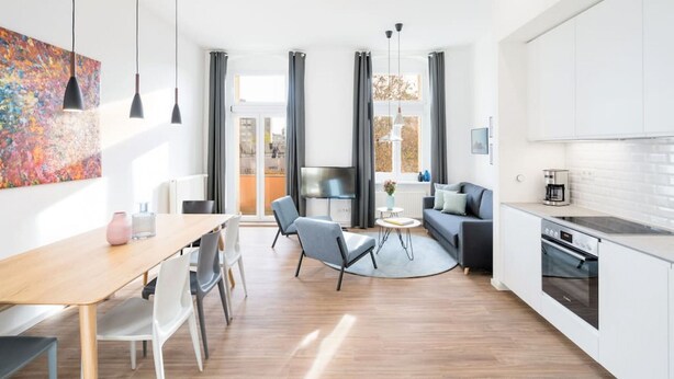 A modern kitchen with white cabinets, a dining area with a wooden table and chairs, and a living area with a sofa and a coffee table.