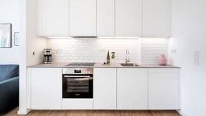 A modern kitchen with white cabinetry, a built-in oven, and a countertop with a coffee maker and a vase.