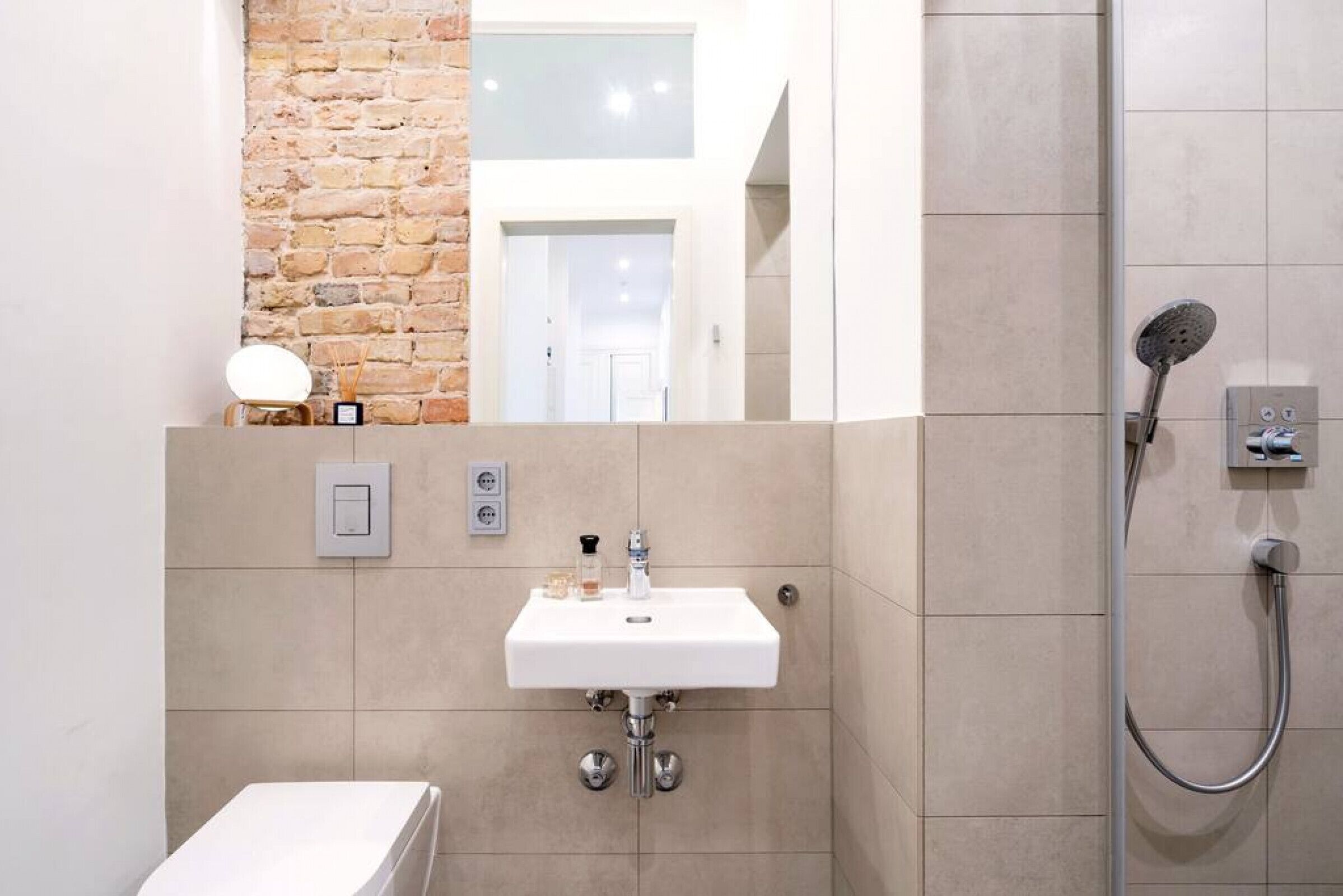 A modern bathroom with a white sink, a shower, and a brick accent wall.