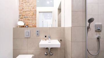A modern bathroom with a white sink, a shower, and a brick accent wall.
