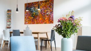 A modern living room with a blue sofa, a round coffee table, and a vase of flowers. There is a dining area with a table and chairs in the background.