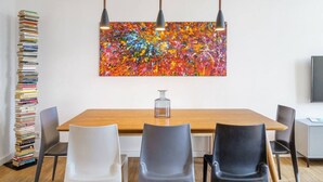 Un comedor moderno con una mesa de madera, tres sillas y un cuadro abstracto de colores.