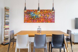 Ein moderner Essbereich mit Holztisch, drei Stühlen und einem farbenfrohen abstrakten Gemälde darüber.