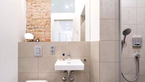 Un baño moderno con un lavamanos blanco, ducha y pared decorativa de ladrillo.