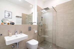 Et moderne badeværelse med hvid vask, toilet og brusekabine i glas.