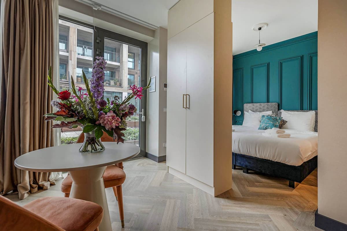 Una camera d'albergo con un letto, un tavolo con un vaso di fiori e vista sul balcone esterno.