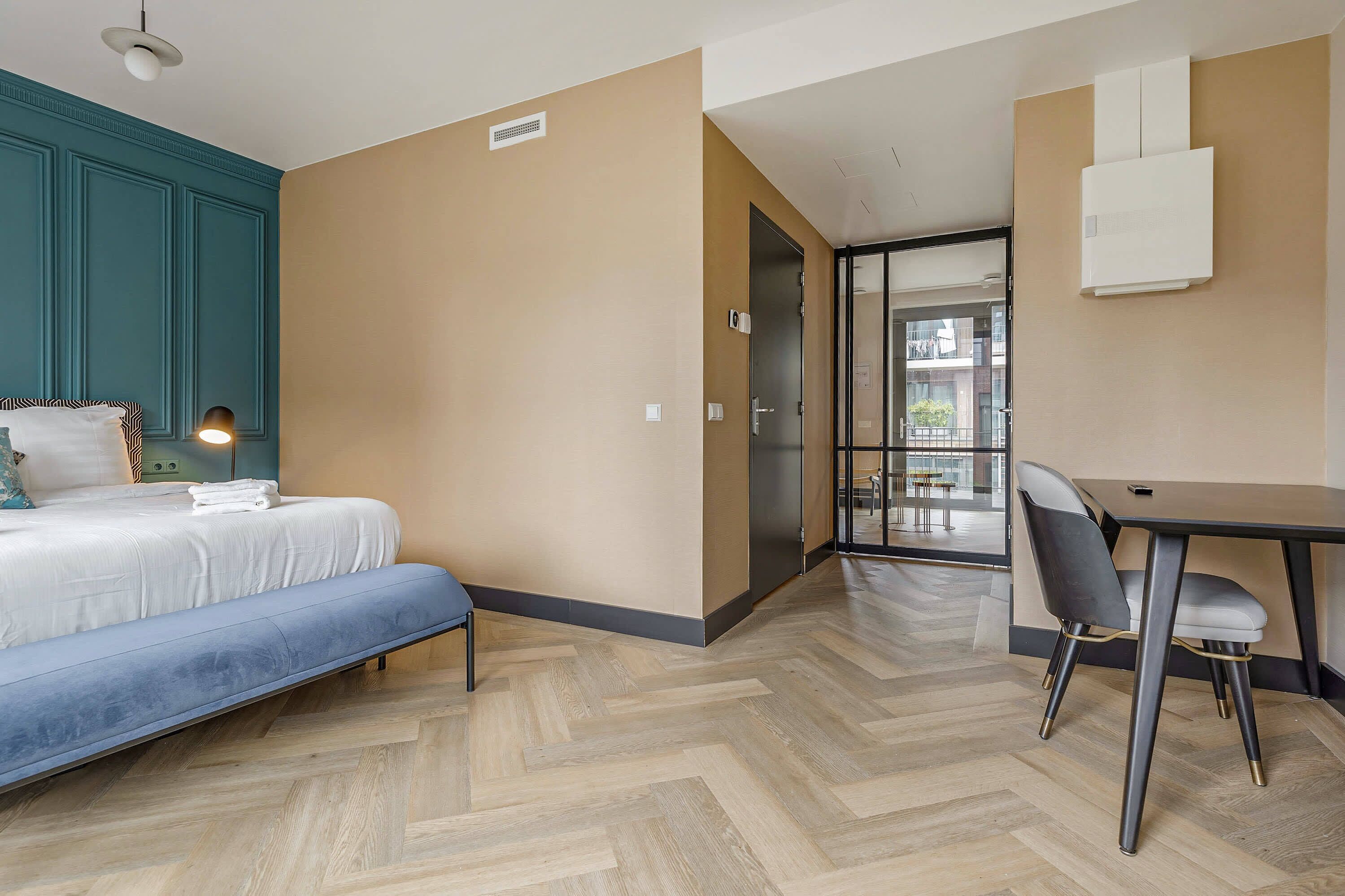 A modern hotel room with a bed, bench, desk, and chair.