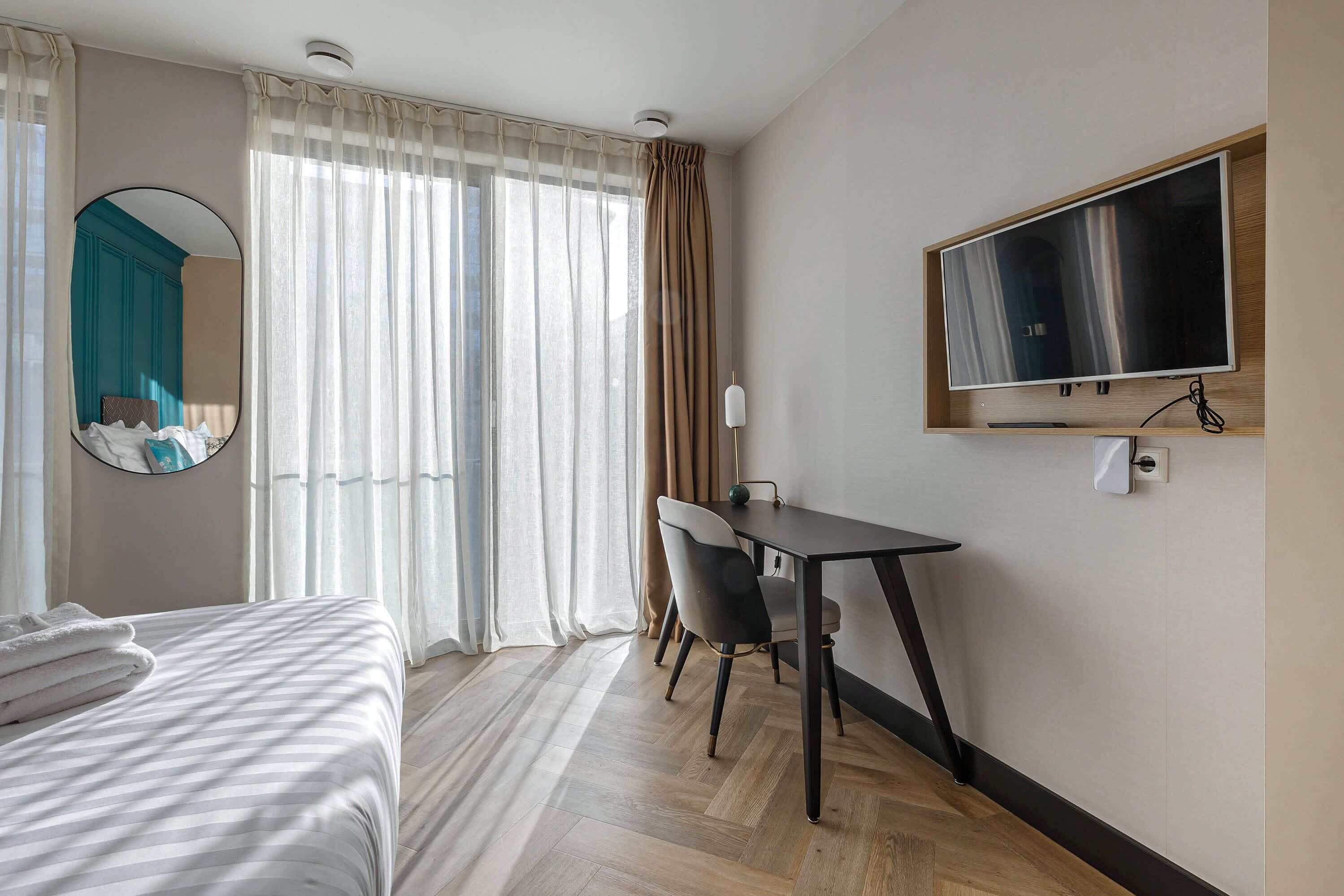 Una habitación de hotel con una cama, un escritorio, una silla, un televisor y una ventana con cortinas.