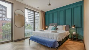 A modern bedroom with a large bed, a bench, a mirror, and a view of the city through large windows. - Bens The Highdocks (Amsterdam)