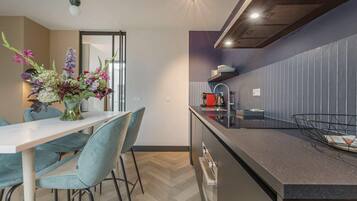 Una cocina moderna con comedor, que presenta un piso de madera en espiga, una isla central con fregadero y un jarrón de flores sobre la mesa.