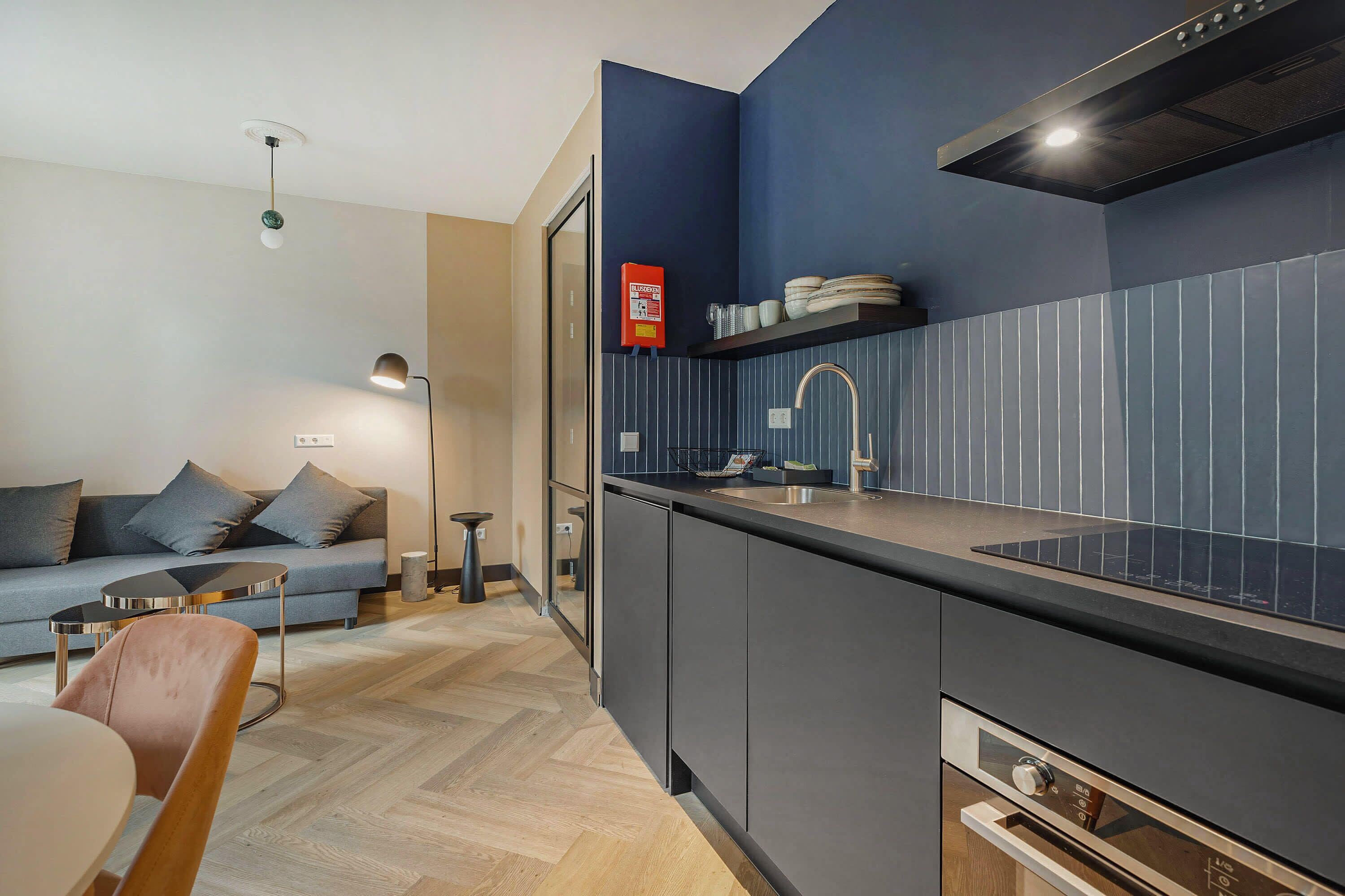 Una cocina moderna con estufa integrada, un lavamanos y una encimera. En el área de estar contigua hay un sofá y una mesa de comedor.