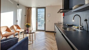 A modern kitchen with a black countertop, stainless steel sink, and a built-in oven. There is a dining area with a round table and two chairs. - Bens The Highdocks (Amsterdam)