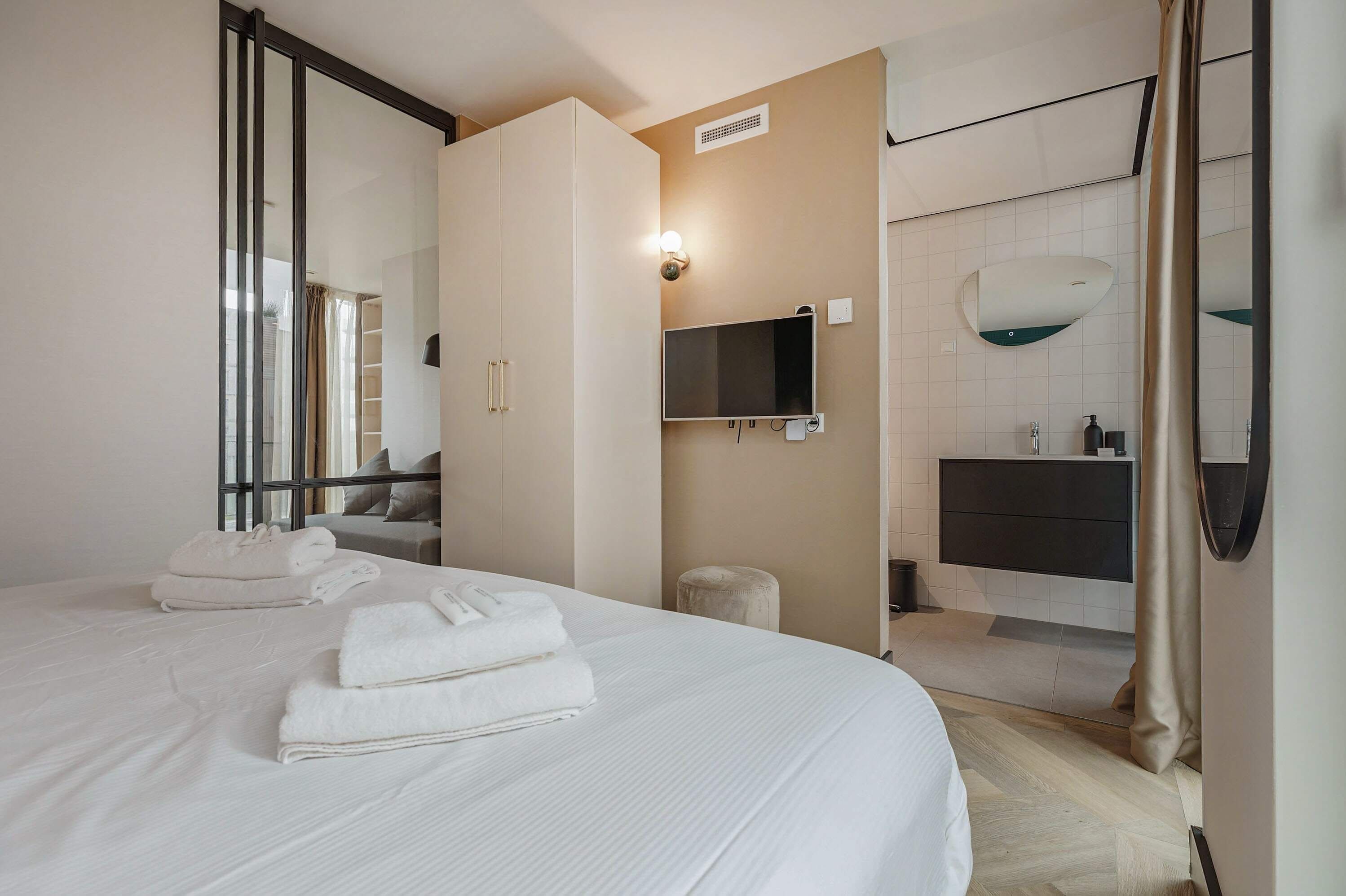 Hotelkamer met een groot bed, een kledingkast, een televisie en een badkamer met spiegel en wastafel.