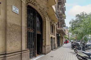 Un edificio histórico con detalles arquitectónicos ornamentales, un cartel que indica 'Casa Bailles 1904', y una acera pavimentada con scooters estacionados.