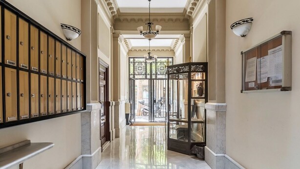 A hallway with lockers, a glass door entrance, a chandelier, and a bulletin board. - Sagrada Familia view in BCN center (Barcelona)