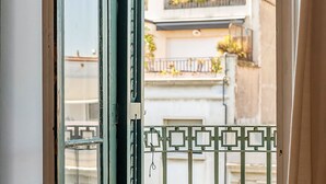 A view through a window with a metal gate, a balcony with plants, and a building facade. - Sagrada Familia view in BCN center (Barcelona)