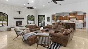 A spacious living room with leather sofas, a fireplace, and a kitchen area with wooden cabinets and a central island. - Chateau Vino - French Style Chalet (Temecula)