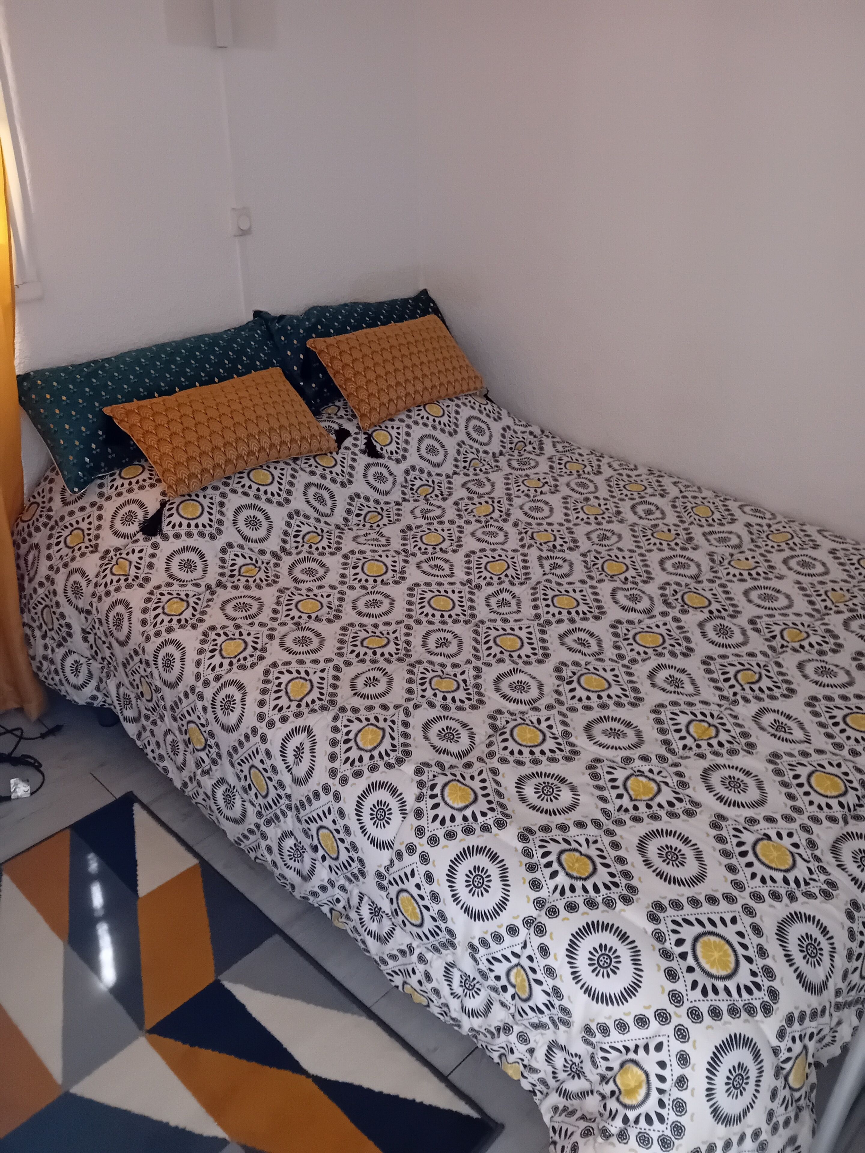A single bed with patterned bedding, two pillows, and a geometric rug.