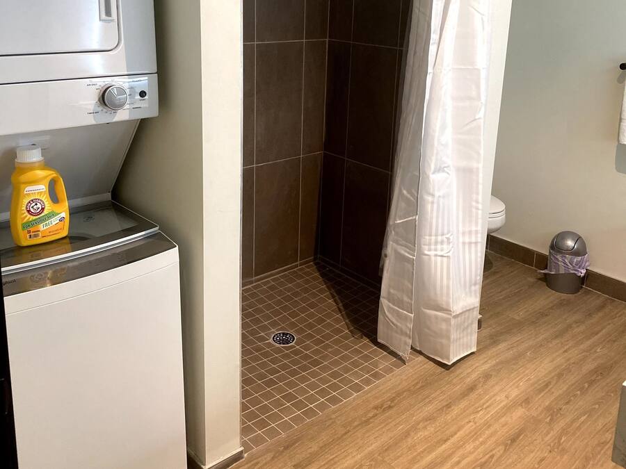 Casa de banho com chuveiro, máquina de lavar roupa e uma embalagem de detergente.