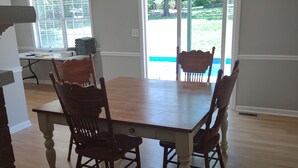 Un comedor con una mesa y sillas de madera, una araña y vista a un patio trasero a través de un ventanal.