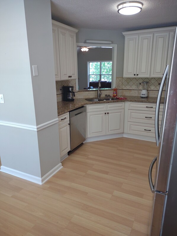 A kitchen with white cabinets, a stainless steel refrigerator, a coffee maker, and a window with a view of greenery.