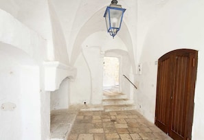 A narrow hallway with white walls, a wooden door, and a stone floor.